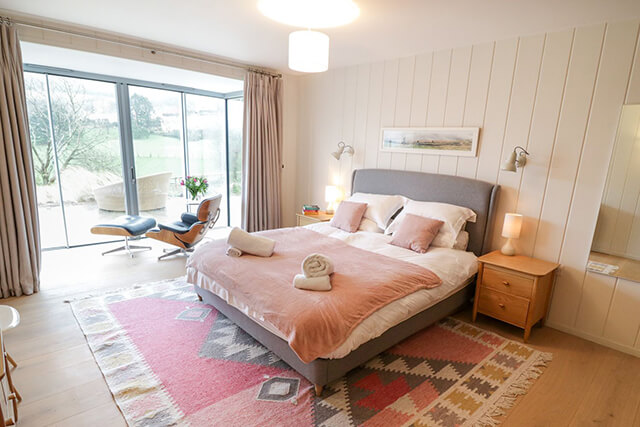 Bedroom at Woodwater with comfy bed, beautiful interior design and a lounge chair to admire the view.