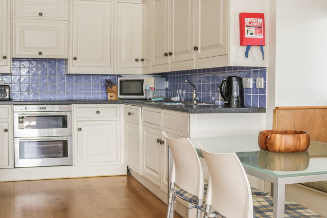 Kitchen with fire blanket, dining table, kitchen appliances and white cupboards.