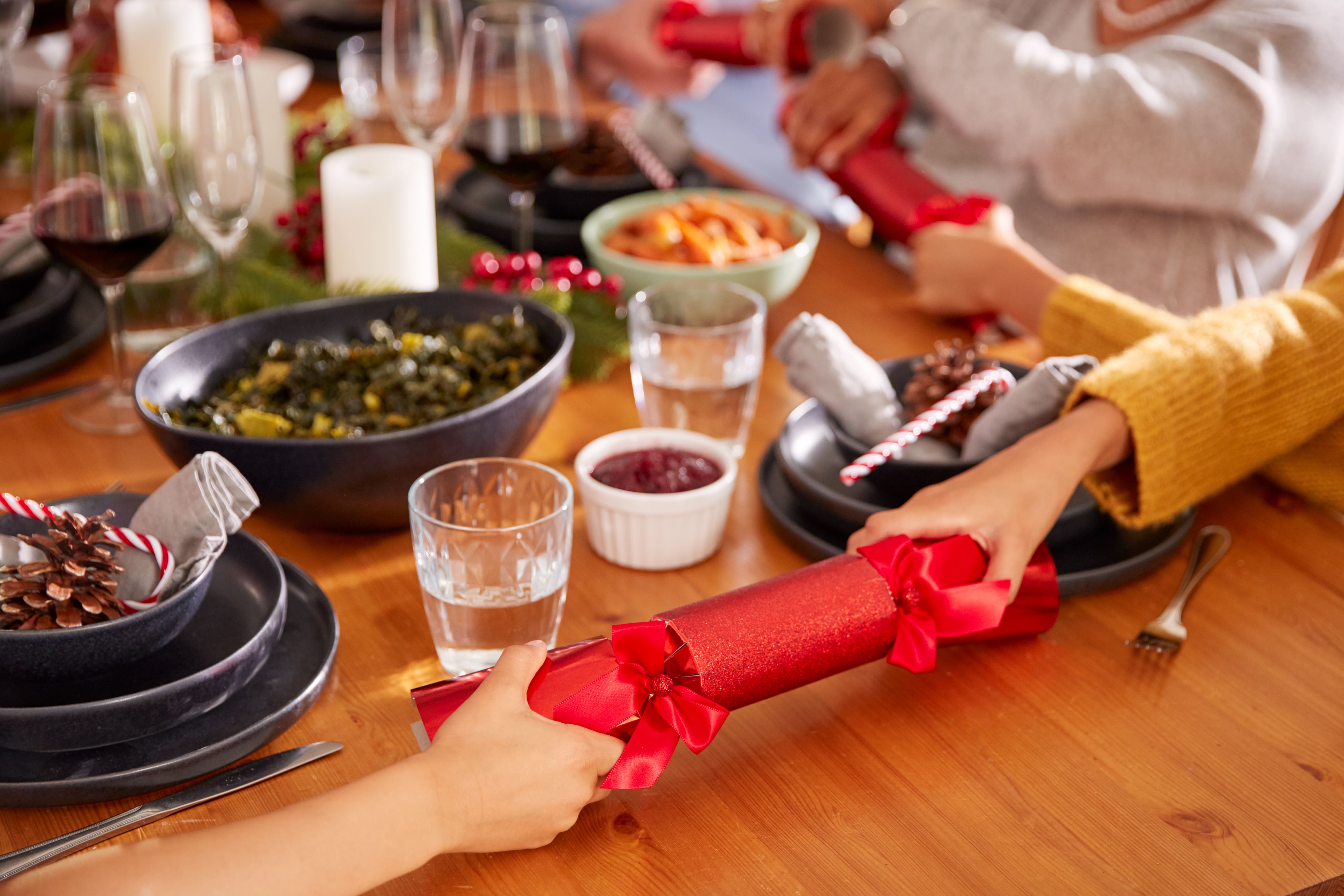 Close-Up-Of-Multi-Generation-Family-Pulling-Christmas-Crackers-As-They-Sit-For-Meal-At-Table