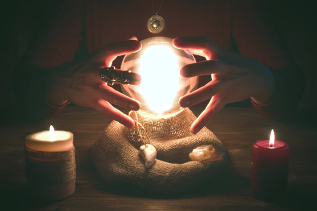 crystal-ball-illuminated-in-seance-with-hands-and-candles-either-side