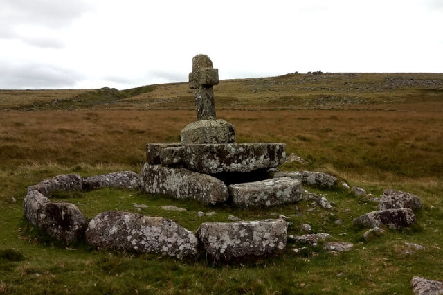 A stone tomb with a stone cross on top of it amidst the Dartmoor landscape. According to Dartmoor legend it is Childe's Tomb.