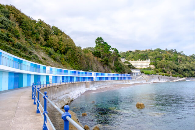 View of Meadfoot Beach in Torquay, Devon with blue beach huts backing the shore.