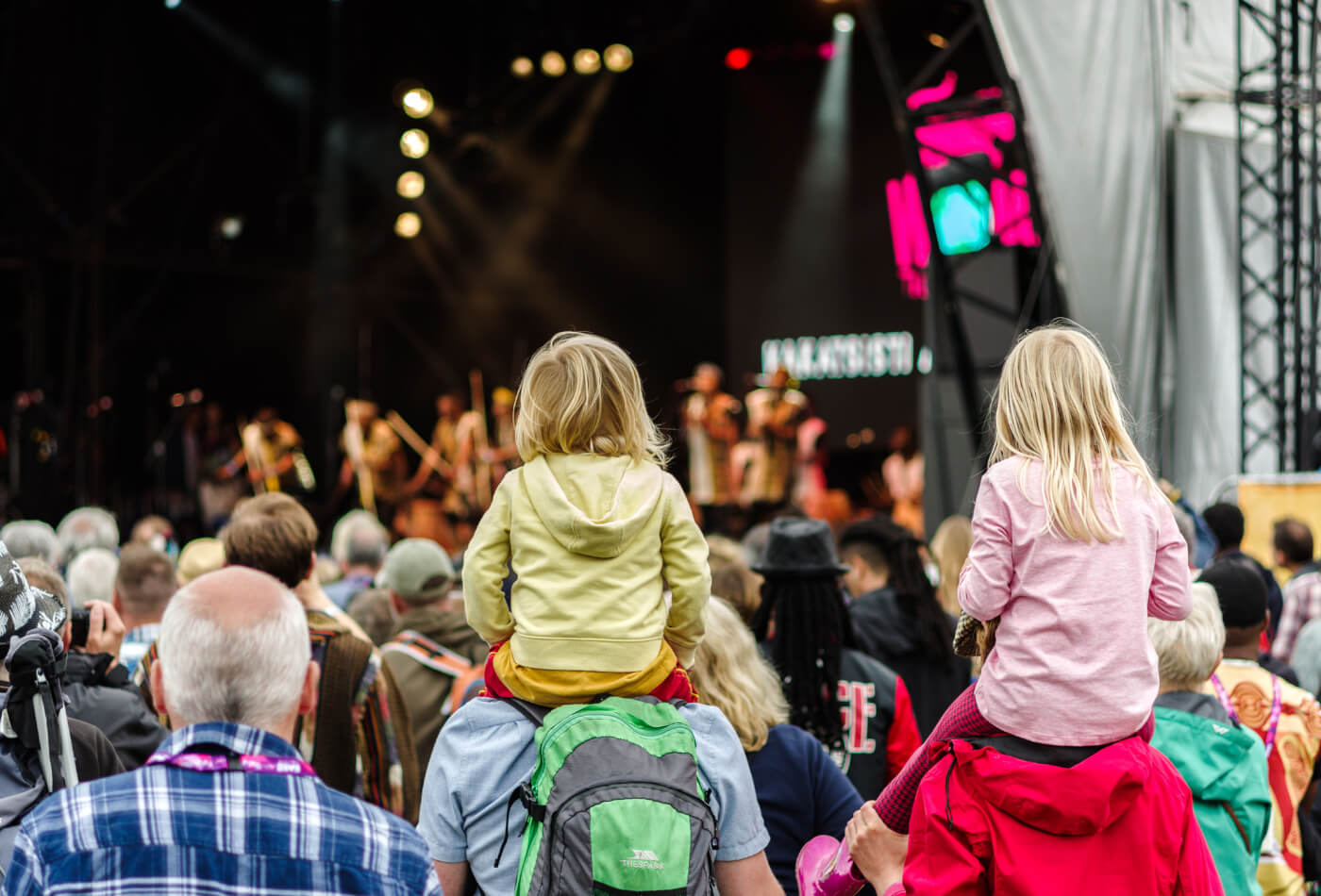 Adults watching live music with children on shoulders.