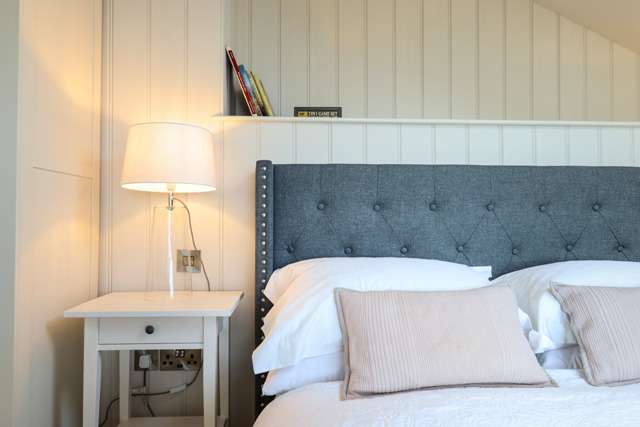 Corner of a double bed with a bed side lamp next to it