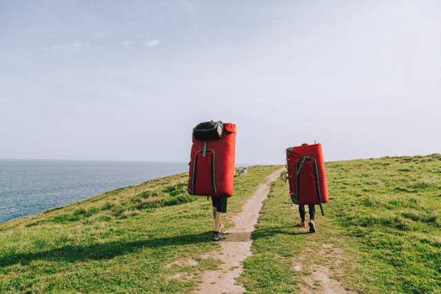 Two climbers carrying boulder pads along the coast.