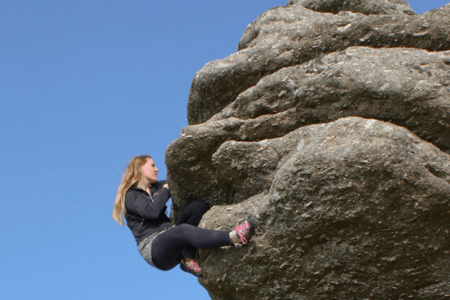 Woman tackles boulder problem at Bonehill Rocks in Dartmoor.