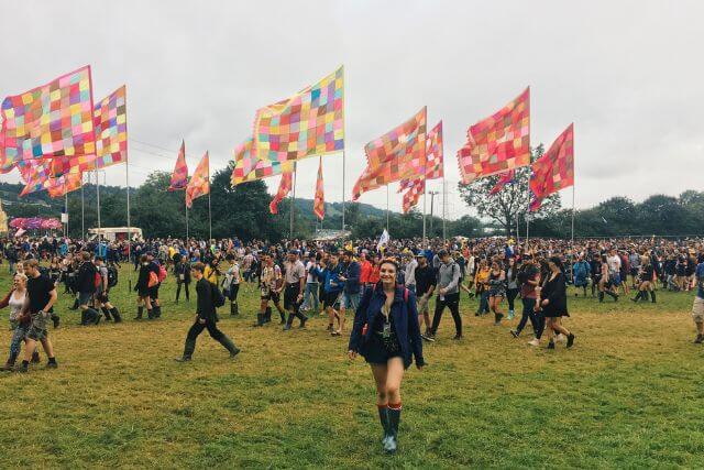 A woman walking towards the camera with festival flags and crowds in the background.