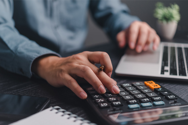 A man using a calculator and laptop to figure out his taxes