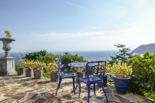 View of the sea from a patio on a sunny day, with blue metal chairs in the foreground.