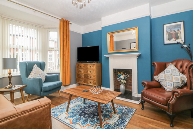 Cosy lounge with a blue feature wall, modern design and a large bay window, at Cornserside, Sidmouth.