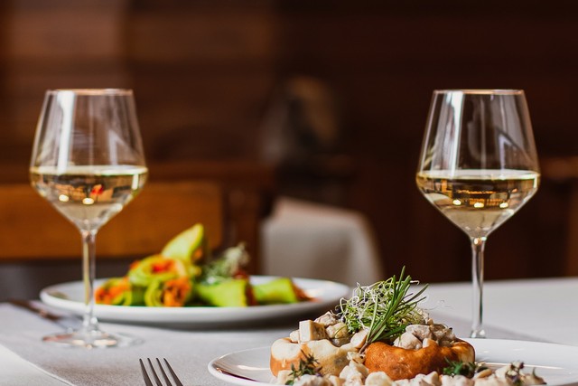 Two meals and glasses of wine on a table with a white table cloth, in a warmly lit restaurant.