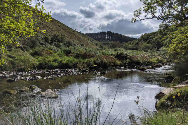 Landscape of the Doone valley in Exmoor, with a river in the foreground and hills and forest further away