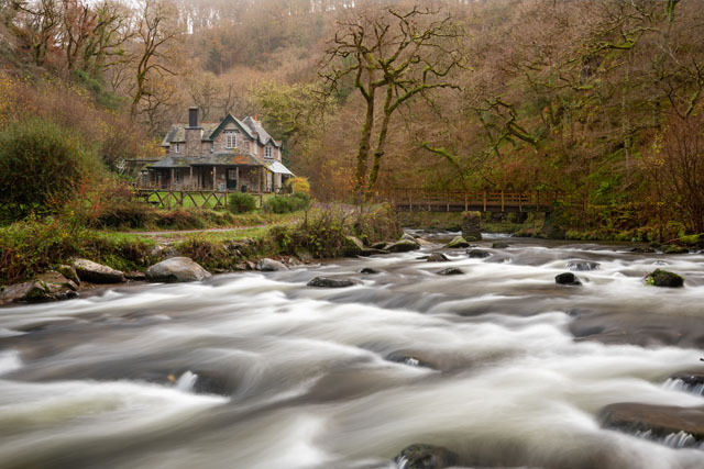View of Watersmeet house surrounded by trees in Autumn, with the East Lyn River in the foreground